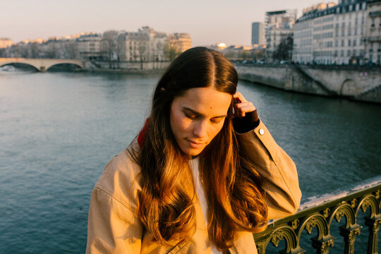 Female traveler stands posing beside the Seine River at sunset