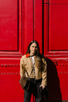 Woman posing in front of a red door on a sunlit street in Paris