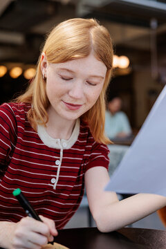 Redhead woman studies, writing with a marker, focused and thoughtful.