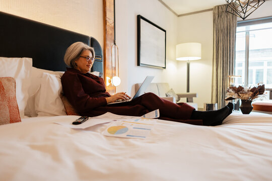 Professional Senior woman using laptop working in hotel room bed
