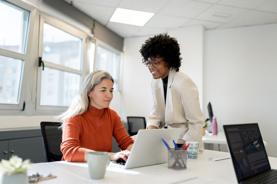 Businesswomen collaborating on laptop in modern office