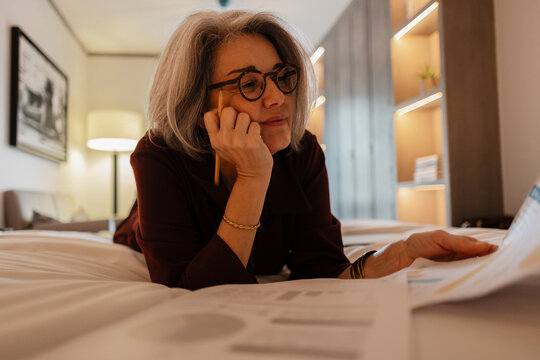Professional woman working with documents and statistics on bed