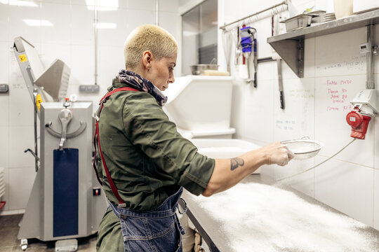 Baker sifting flour preparing dough in commercial kitchen