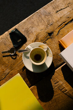 Empty coffee cup beside sunglasses, books, and a hotel room key
