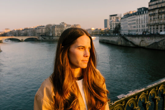 A woman traveling through Paris pauses by the Seine at dusk