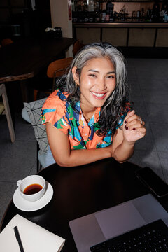 Smiling woman works at cafe with coffee and laptop.