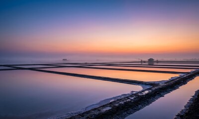 Obraz premium Wide landscape photograph of traditional Thai salt flats at dawn, perfectly still shallow brine water creating flawless mirror reflection of dramatic pastel sky with gradient.