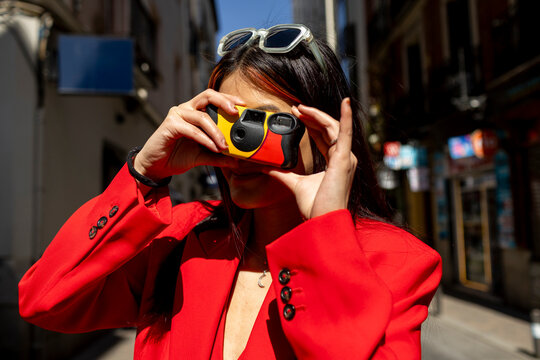 smiling woman taking a photo with disposable camera in city street