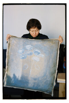 A woman holds a large canvas with a floral design in her hands.