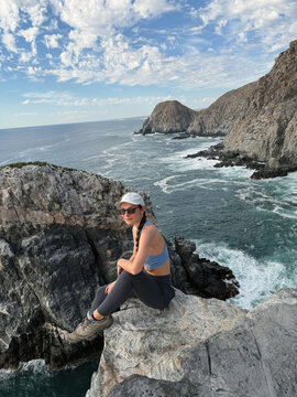 woman in sport apparel sits on a cliff by the rocky shore