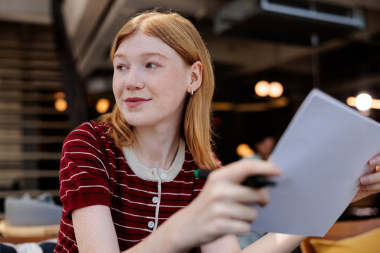 Redhead with paper and pen looks thoughtfully away.