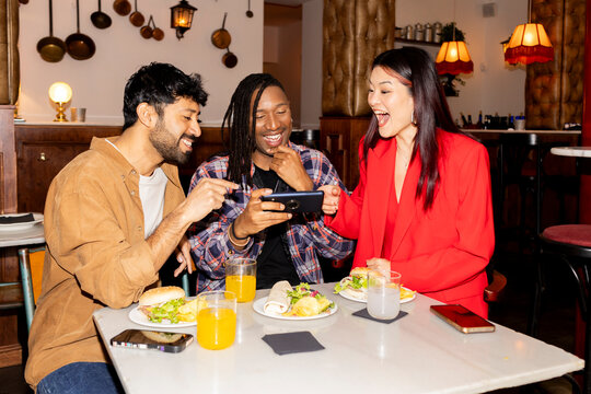 Group of Friends at restaurant checking smartphone laughing. 