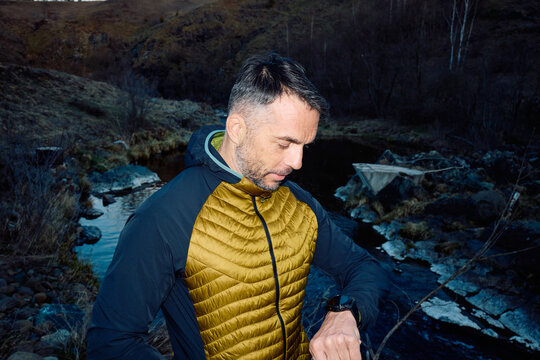 Man stands by the mountain creek, checks his watch