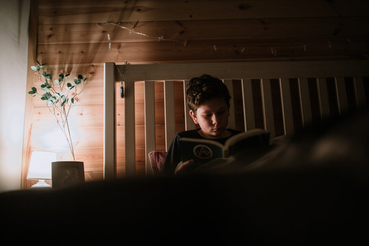 Boy reading a book at night in the bed. 