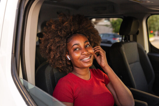 Smiling black woman with afro hair and earbuds inside a car