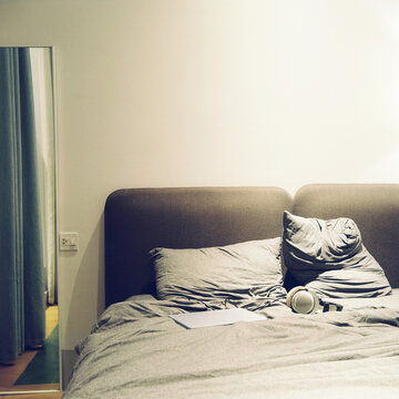 Cozy bedroom with unmade bed, pillows, headphones, and papers