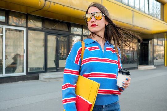 Stylish woman walking with coffee and documents in urban setting