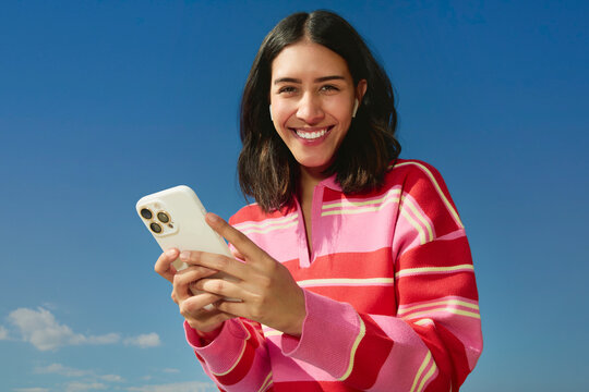 Woman using smartphone outdoors smiling under blue sky