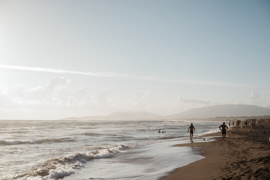 People walking along the shoreline on a wide beach at sunset