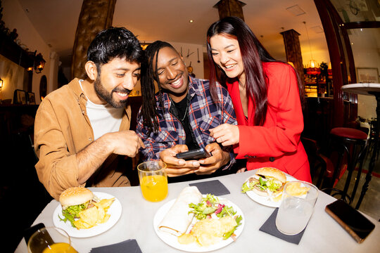 Group of Friends at restaurant checking smartphone laughing. Fisheye.