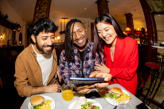 Group of Friends at restaurant checking smartphone laughing. Fisheye.