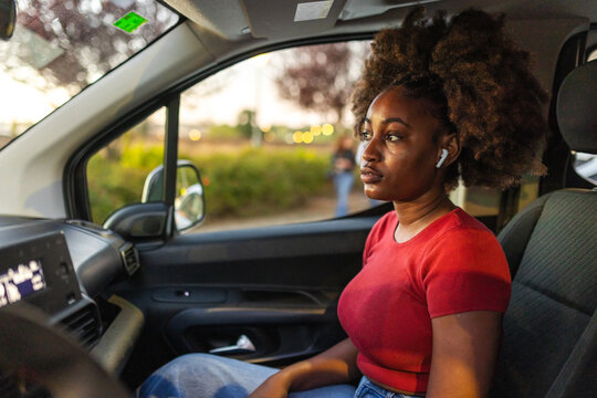 Black woman with afro hair and earbuds looking out of a car window