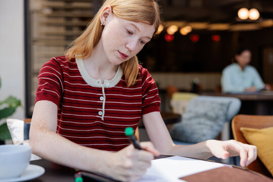 Woman writing on paper at outdoor cafe table.