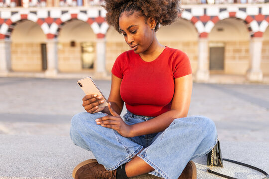Young black woman with afro hair using a smartphone outdoors