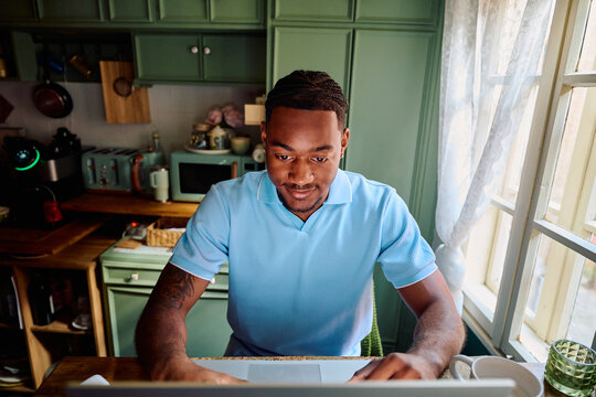 Young Black Man Working on Laptop at High Table in Kitchen
