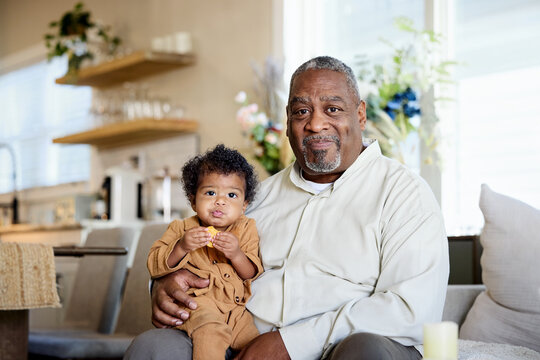A Grandfather Sits on a Couch Holding His Grandson