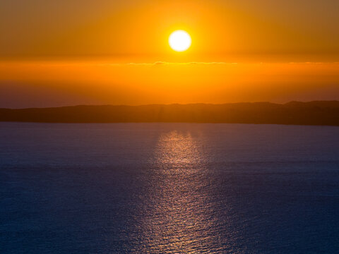 Setting Sun sinking into a cloud bank and reflecting on a dark ocean