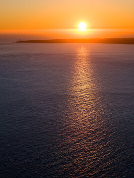 Setting Sun sinking into a cloud bank and reflecting on a dark ocean