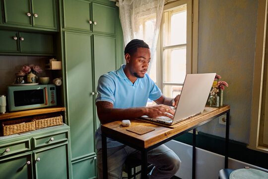 Young Black Man Working on Laptop at High Table in Kitchen