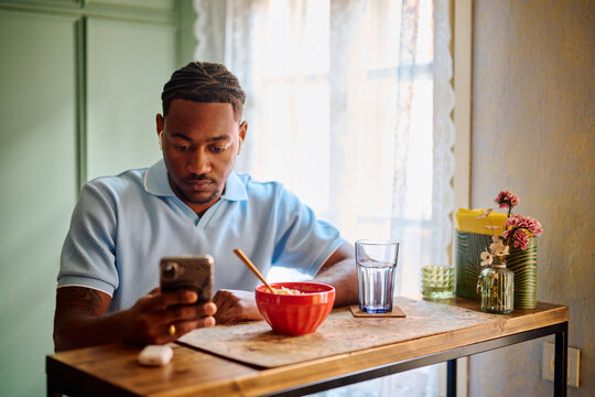 Young Black Man Checking Smartphone During Break in Kitchen