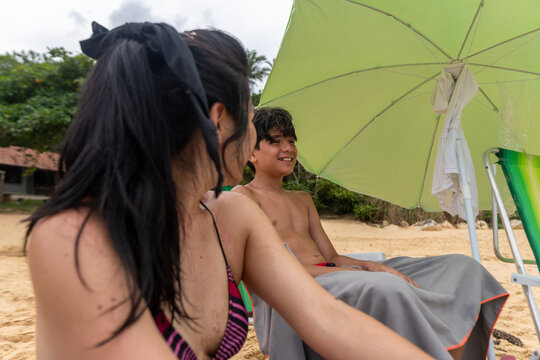 Two people enjoy time on the beach under a large umbrella