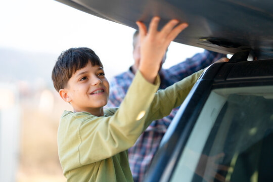 Young boy helps load items onto car roof