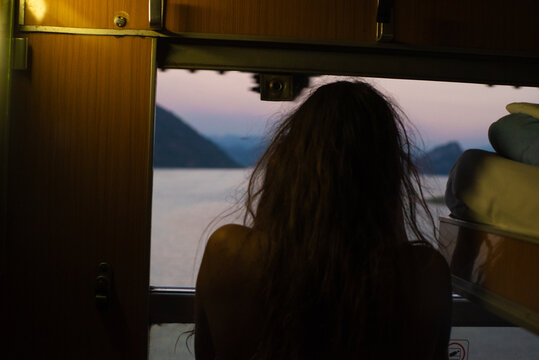 Woman looking through train window at dusk mountain landscape