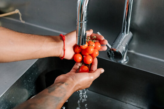 Hands wash cherry tomatoes under running kitchen water