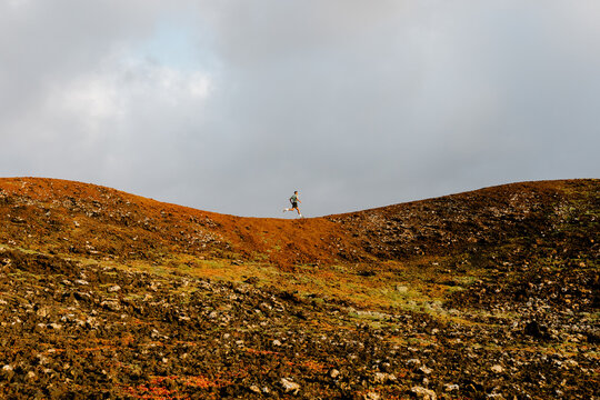A distant trail runner training along a rocky volcanic mountain path