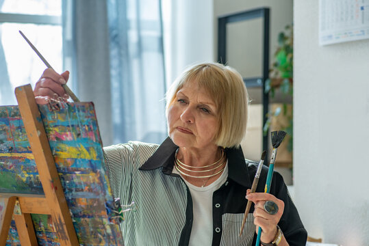 Elderly woman artist drawing on easel in workshop. Close-up to face