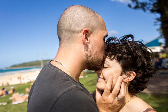 Man kissing woman on forehead with short hair under blue sky