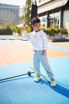 Asian boy standing by a sports net on an outdoor blue court.