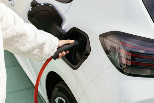 Hand plugging charging cable into electric vehicle charging port