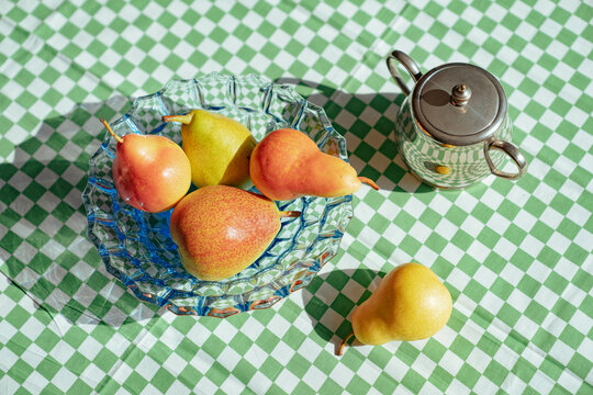 Pears and sugar pot on a green checkered tablecloth in sunlight