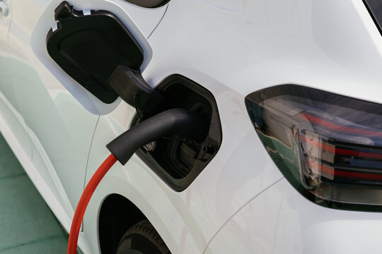 White electric car charging its battery with red cable