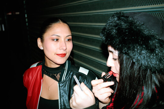 Friends applying lipstick at night