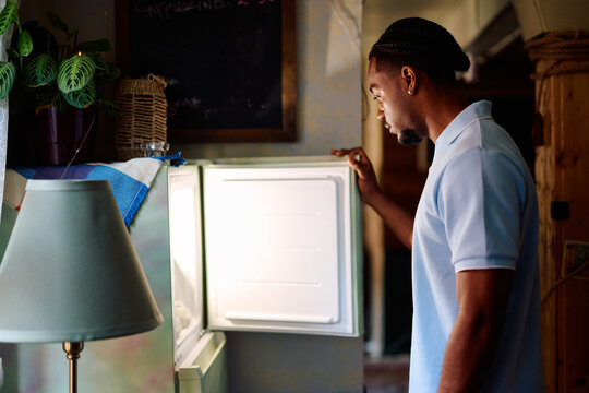 Young Black Man Looking for Food in Open Refrigerator at Home