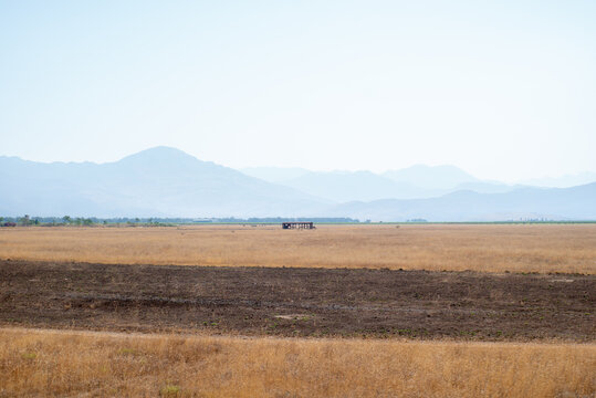 Dry field with distant mountains under hazy sky