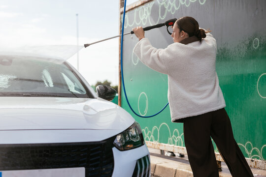 Woman washing white car with high pressure cleaner