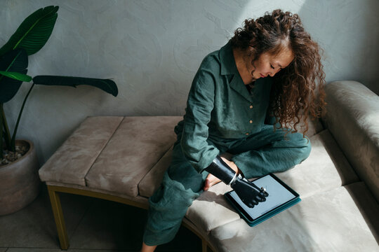 Woman With Robotic Arm Focuses on Digital Tablet in Cozy Setting
